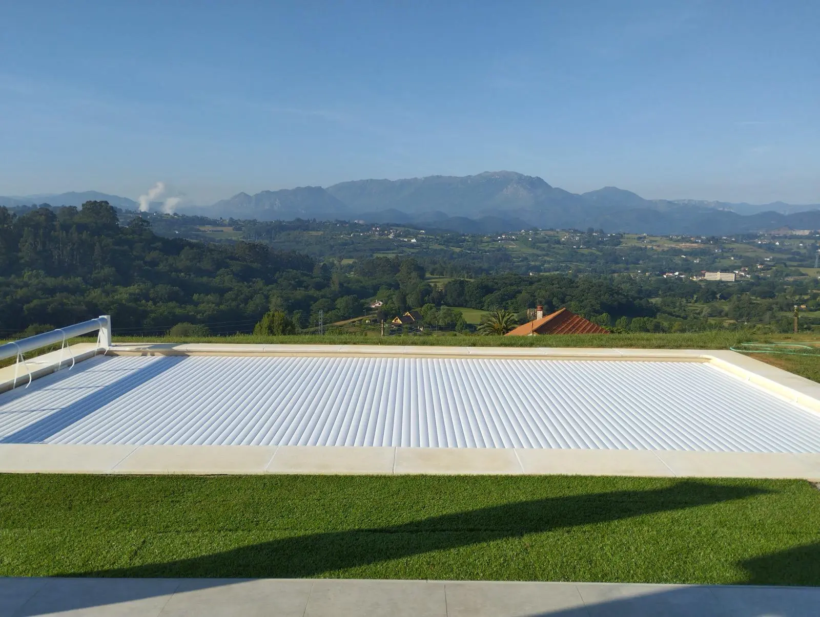 Piscina con cubierta automática de lamas y enrollador elevado, junto a un paisaje de montañas